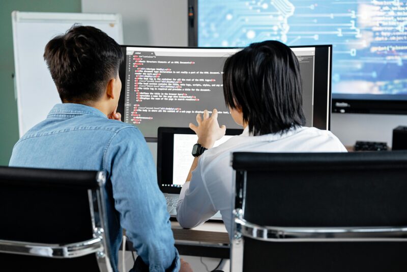 Picture of two young men looking at code on a computer screen.